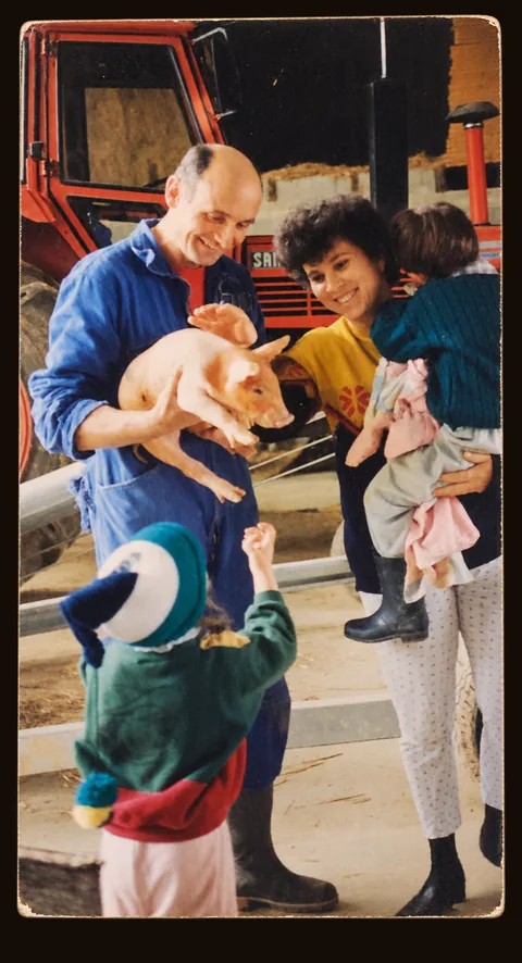 Notre père tenant un porcelet, notre mère et deux des enfants devant le tracteur de la ferme